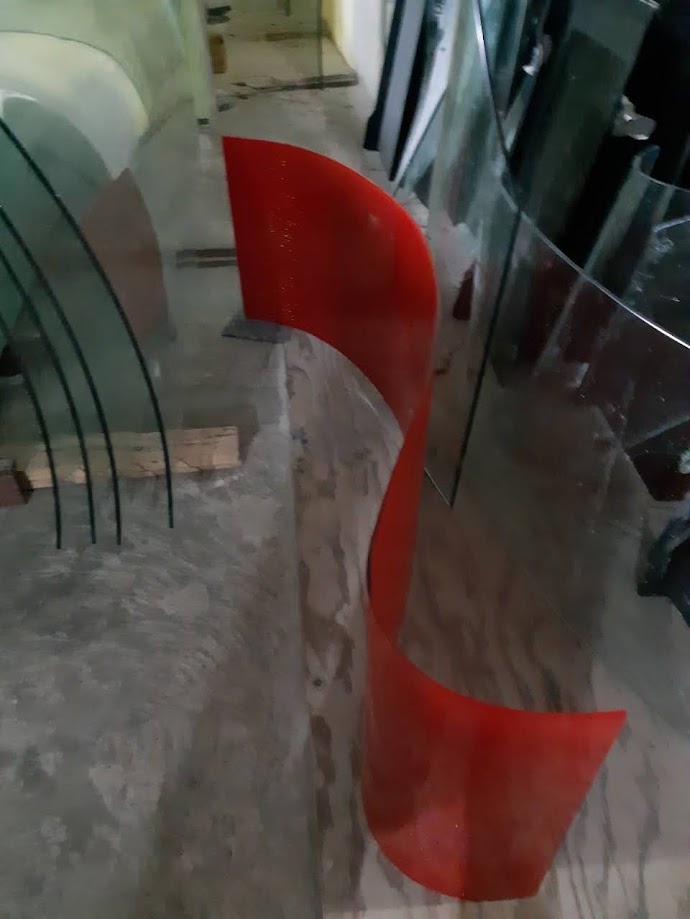 Tấm mica đỏ uốn cong đặt cạnh các tấm kính cong trong xưởng gia công kính nhựa